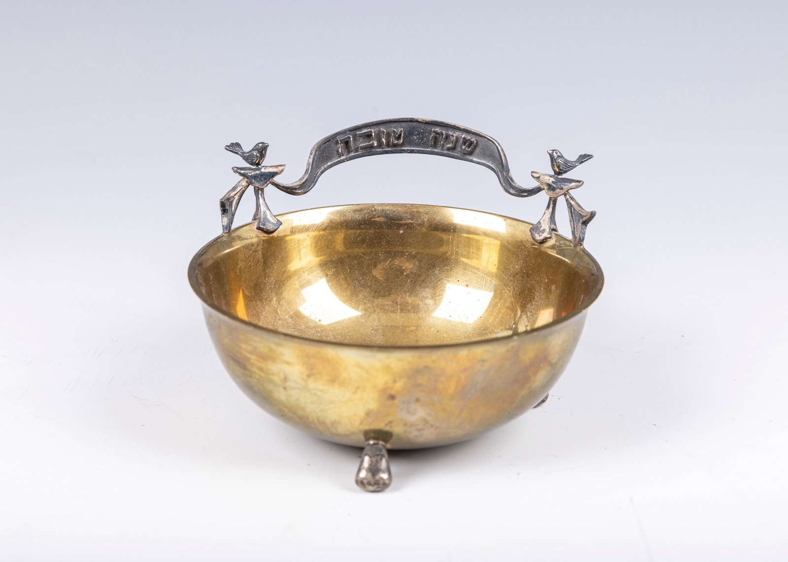 32. A STERLING AND BRASS HONEY DISH BY DUDEK SWED. Jerusalem, 1996. On three silver feet. With two: 32. A STERLING AND BRASS HONEY DISH BY DUDEK SWED. Jerusalem, 1996. On three silver feet. With two birds holding up a ribbon. 4â€? wide.