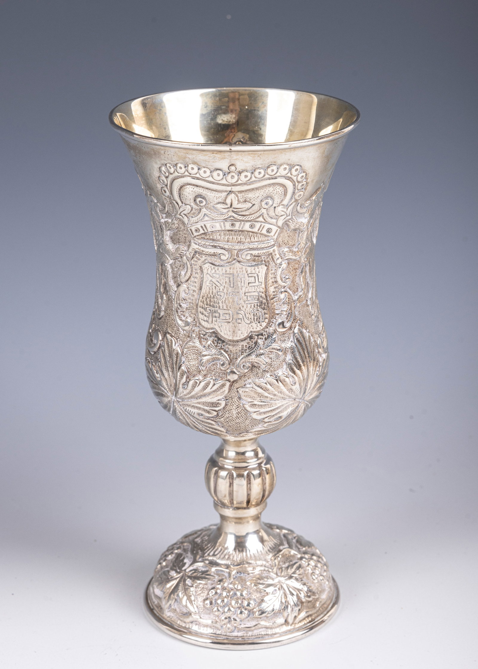 92. A LARGE SILVER KIDDUSH GOBLET. Probably Portugal, c. 1980. In traditional form. Embossed with: 92. A LARGE SILVER KIDDUSH GOBLET. Probably Portugal, c. 1980. In traditional form. Embossed with floral and grape designs. The center cartouche with a partial blessing over wine. 7.2" tall and 190.8 