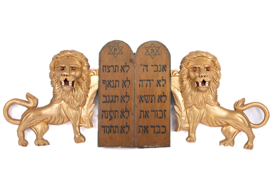 A PAIR OF WOODEN TORAH ARK LIONS. American, early 20th century. Hand carved lions with red eyes flan: A PAIR OF WOODEN TORAH ARK LIONS. American, early 20th century. Hand carved lions with red eyes flanking a painted Decalogue. 38” x 16”.