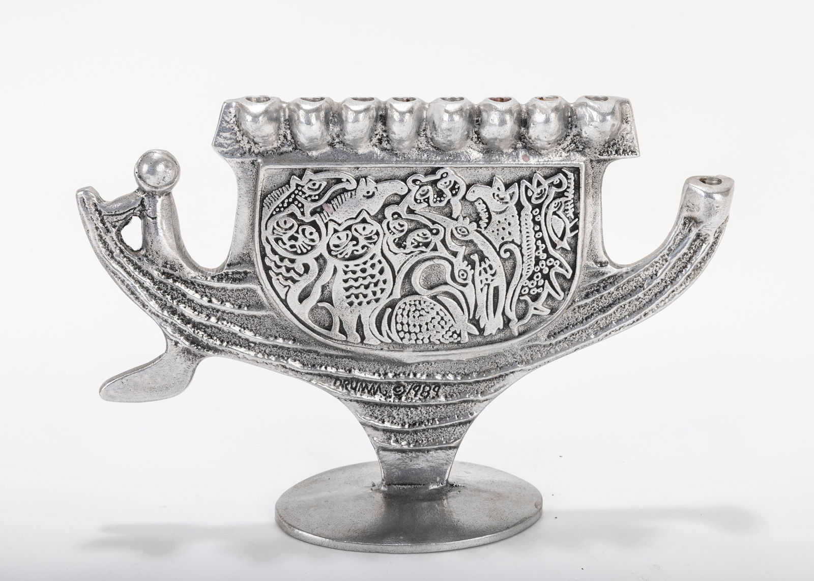 AN ALUMINUM MENORAH SCULPTURE BY DON DRUMM (American, b. 1935).: A ALUMINUM MENORAH SCULPTURE BY DON DRUMM (American, b. 1935). With an ark shaped base, on an oval base. Signed. 10 inches wide. Estimate $200 - 400
