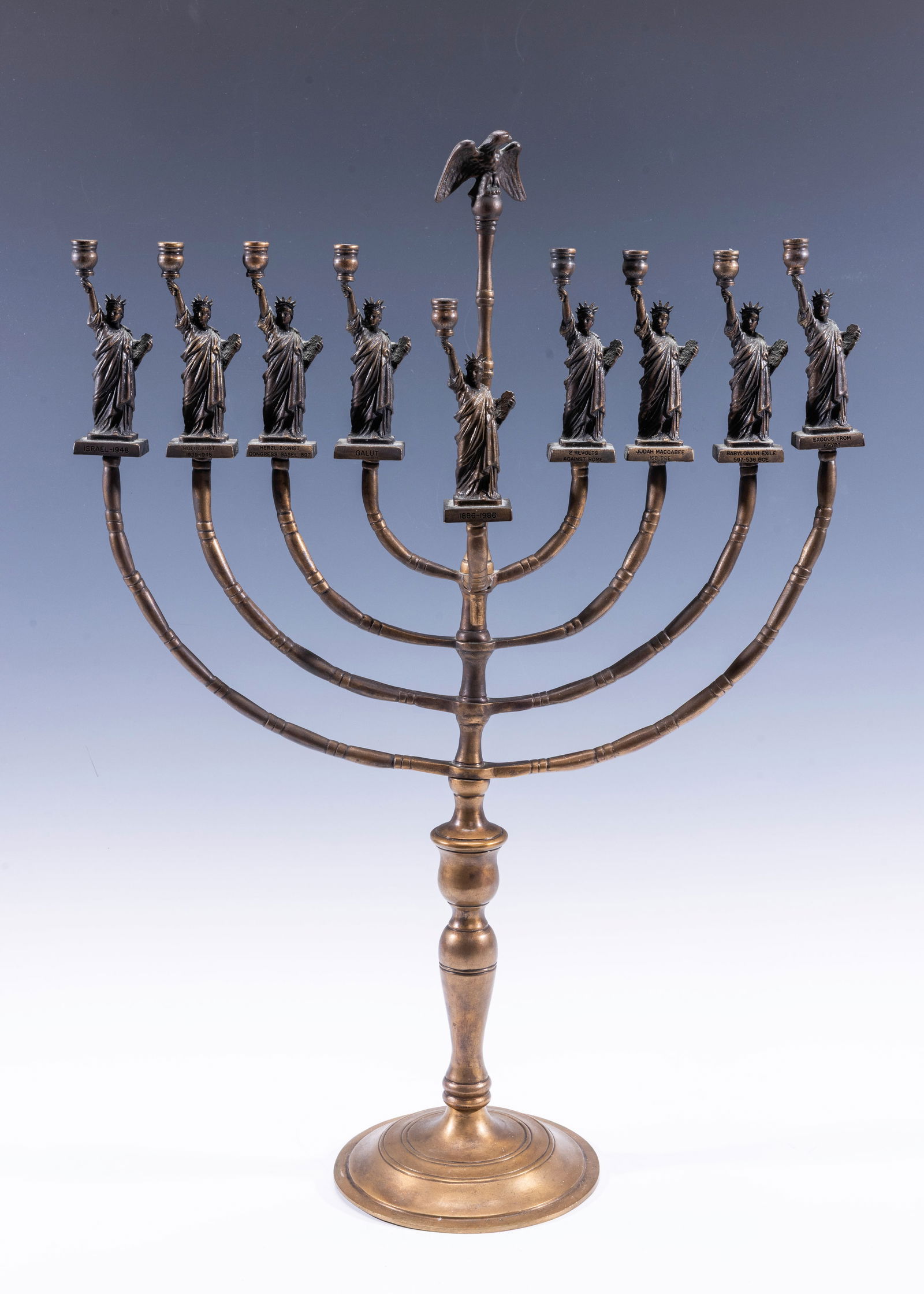 A RARE AND IMPORTANT HANUKKAH MENORAH BY MANFRED ANSON. Bergenfield, New Jersey, c. 1980.: A RARE AND IMPORTANT HANUKKAH MENORAH BY MANFRED ANSON. Bergenfield, New Jersey, c. 1980. On a round base. Each candle holder is in the shape of a miniature statue of liberty, with a different event i