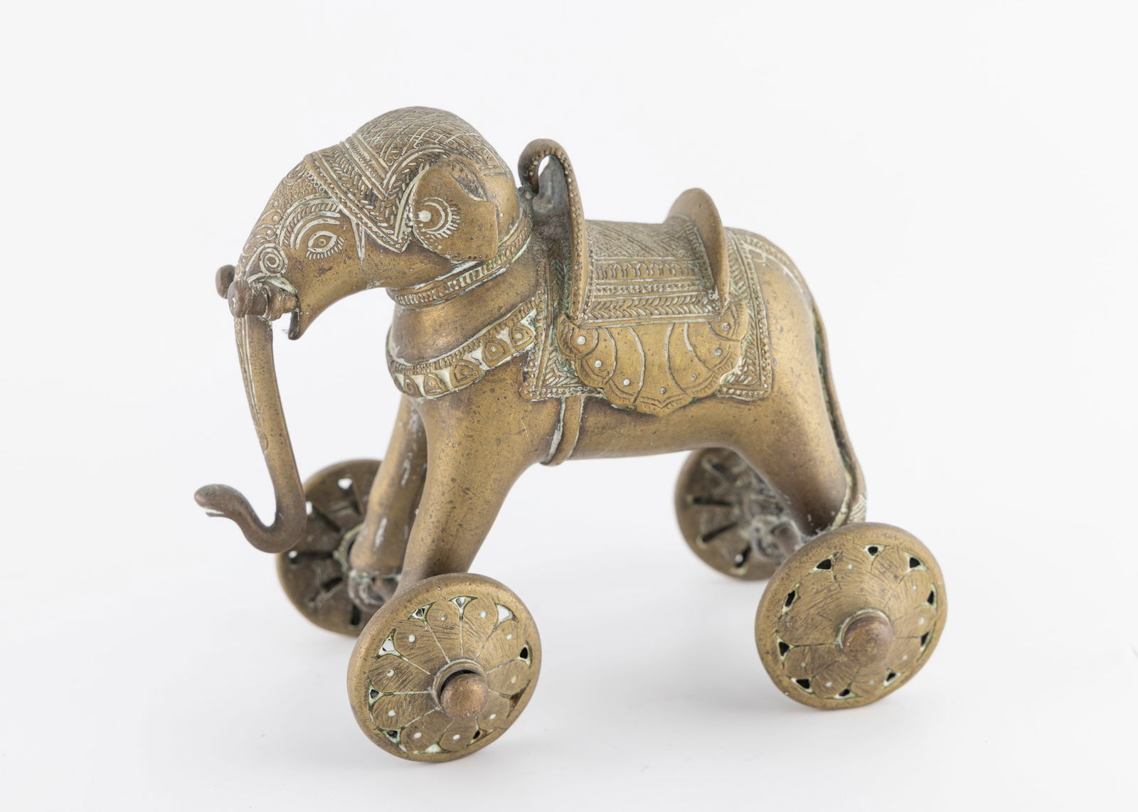 AN EARLY 20TH CENTURY BRASS ELEPHANT. India, c. 1900: On four wheels. Hand engraved in period decoration of a dressed elephant with an extended tusk. 5.9" tall.