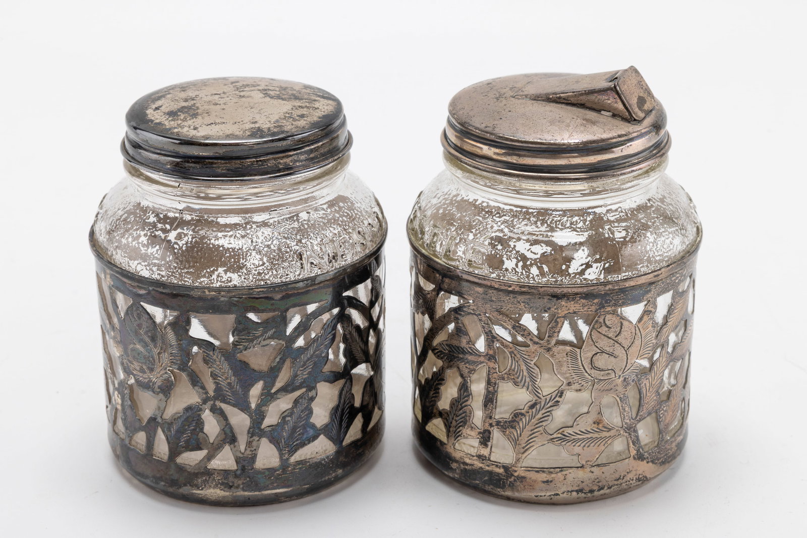 A PAIR OF STERLING SILVER AND GLASS COVERED JARS. Mexico, mid-century.: Glass jars with sterling silver lattice work overlay. 3.9" tall