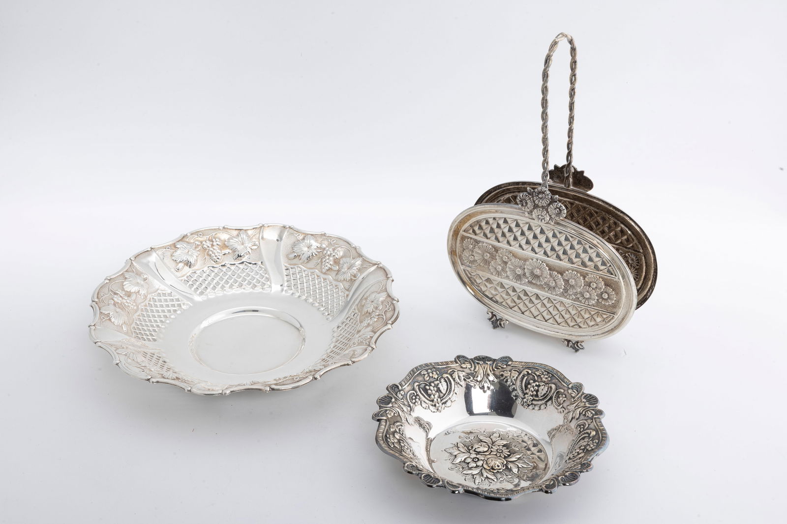 A STERLING SILVER NAPKIN HOLDER AND BOWLS. Probably Israel or Italy, modern.: On four legs. Wth oval shaped embossed sides and a handle (10" tall). Accompanied by two embossed sterling silver bowls. (6" and 9"). Total weight is 508.5 grams.
