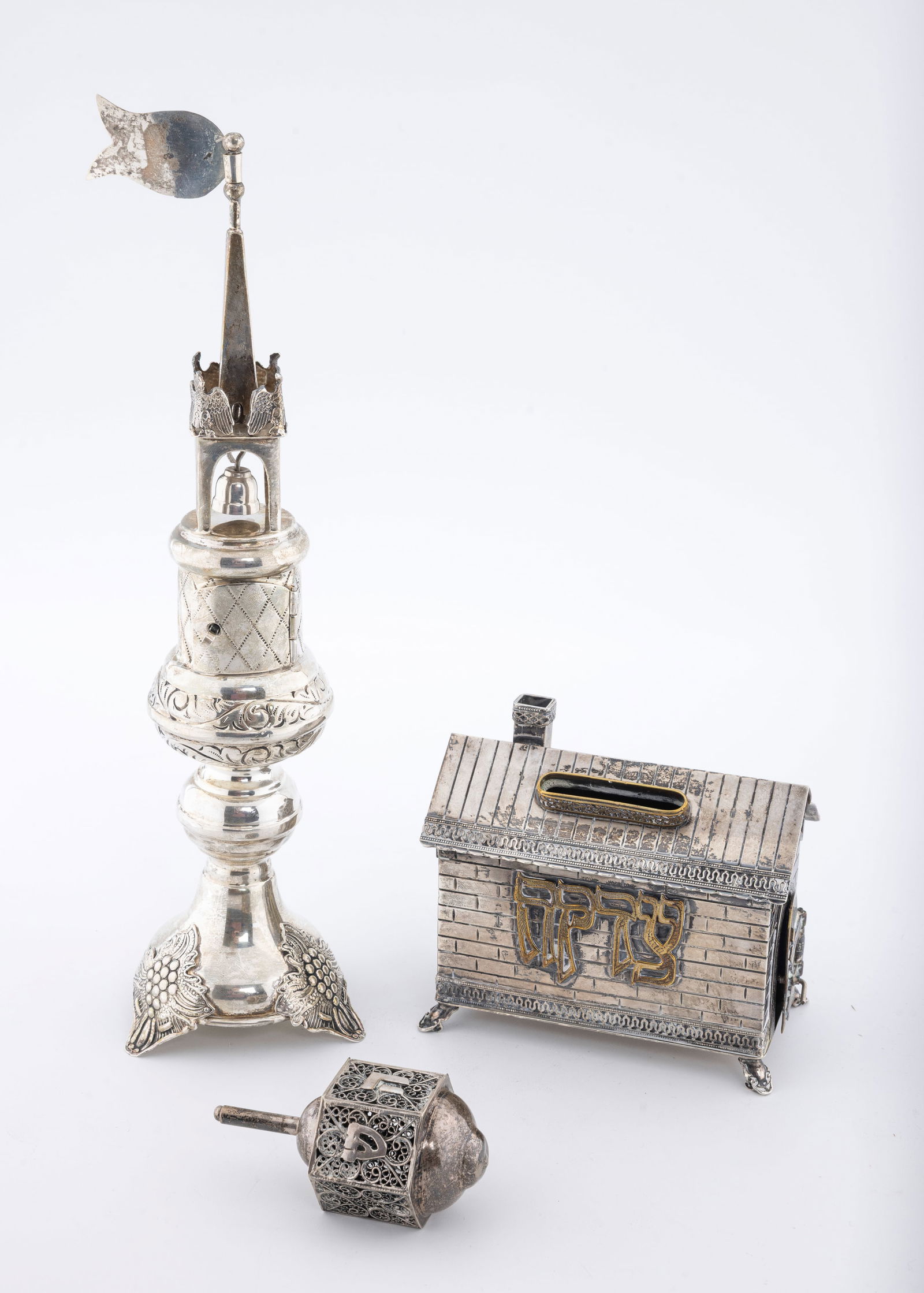 A GROUP OF STERLING SILVER JUDAICA: SPICE BOX, CHARITY BOX AND DREIDEL: The spice box (11" tall) is modern, but in Polish spool form. The charity box (4.2" wide) in the shape of a home. There is some brass overlay. The dreidel (3.1" tall) is filigree. 455 grams