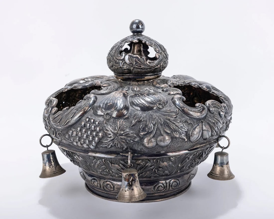 A SILVER TORAH CROWN. Hungarian, 20th century.: A SILVER TORAH CROWN. Hungarian, 20th century. Chased with fruits, scrolls and other organic designs. Fitted with six large silver bells. Inscribed with Hebrew dedication. 11" wide. Similar sold: J. G