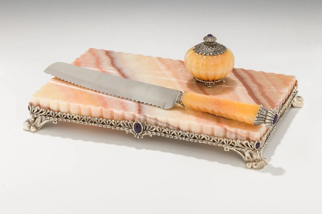 A POLISHED STONE AND STERLING SILVER CHALLAH SET BY YOSEF RODGERO: Jerusalem, modern. Consisting of a Challah knife (13”), a salt cellar and a challah board ( 11.5” x 7”). Signed. Yosef is an Italian Jewish silversmith living in Jerusalem