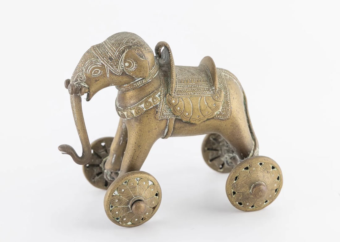 AN EARLY 20TH CENTURY BRASS ELEPHANT. India, c. 1900: On four wheels. Hand engraved in period decoration of a dressed elephant with an extended tusk. 5.9" tall.