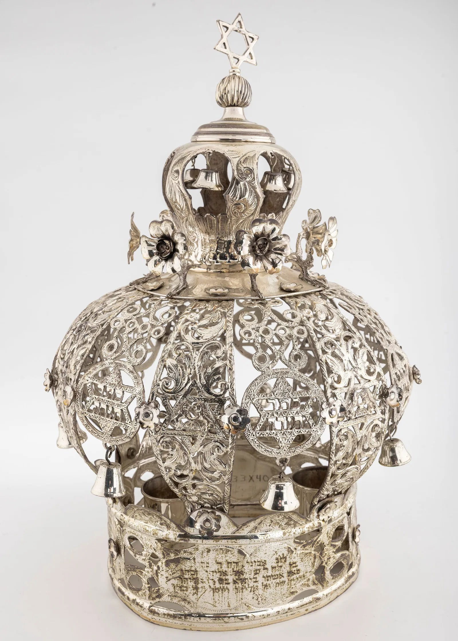 A MASSIVE STERLING SILVER TORAH CROWN. American, early 20th century.: Traditional in shape with sliding staves and multiple ribs seperated by Jewish stars, each indicating "Keter Torah". Engraved with a dedication in Hebrew. Marked Esco, Sterling and hand chased. 66
