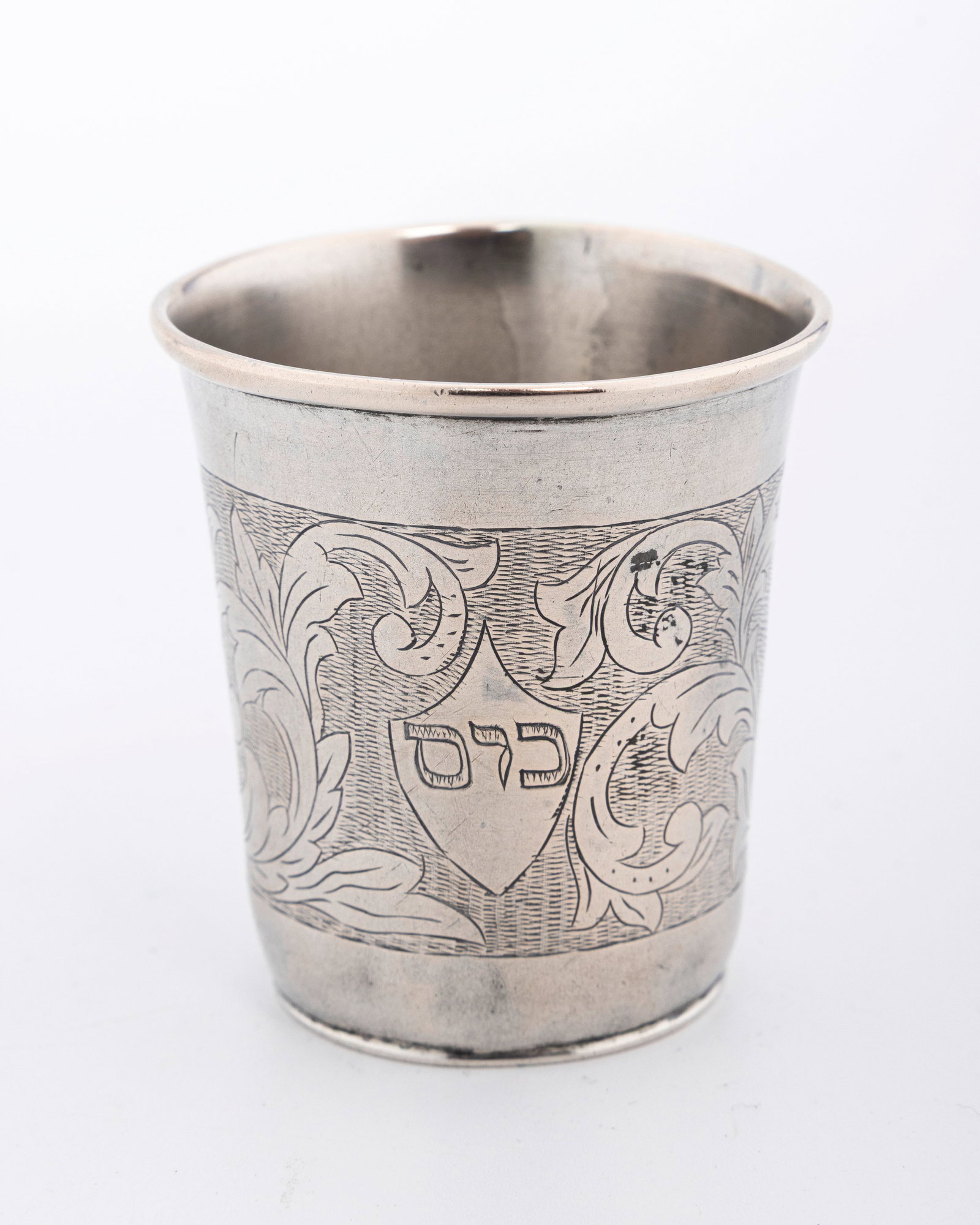 A SILVER KIDDUSH BEAKER. Poland, c. 1820: Tradtional beaker form. Decorated with organic engraved designs. engraved with the word "cup" in Hebrew. 2.1" tall. marked 12
