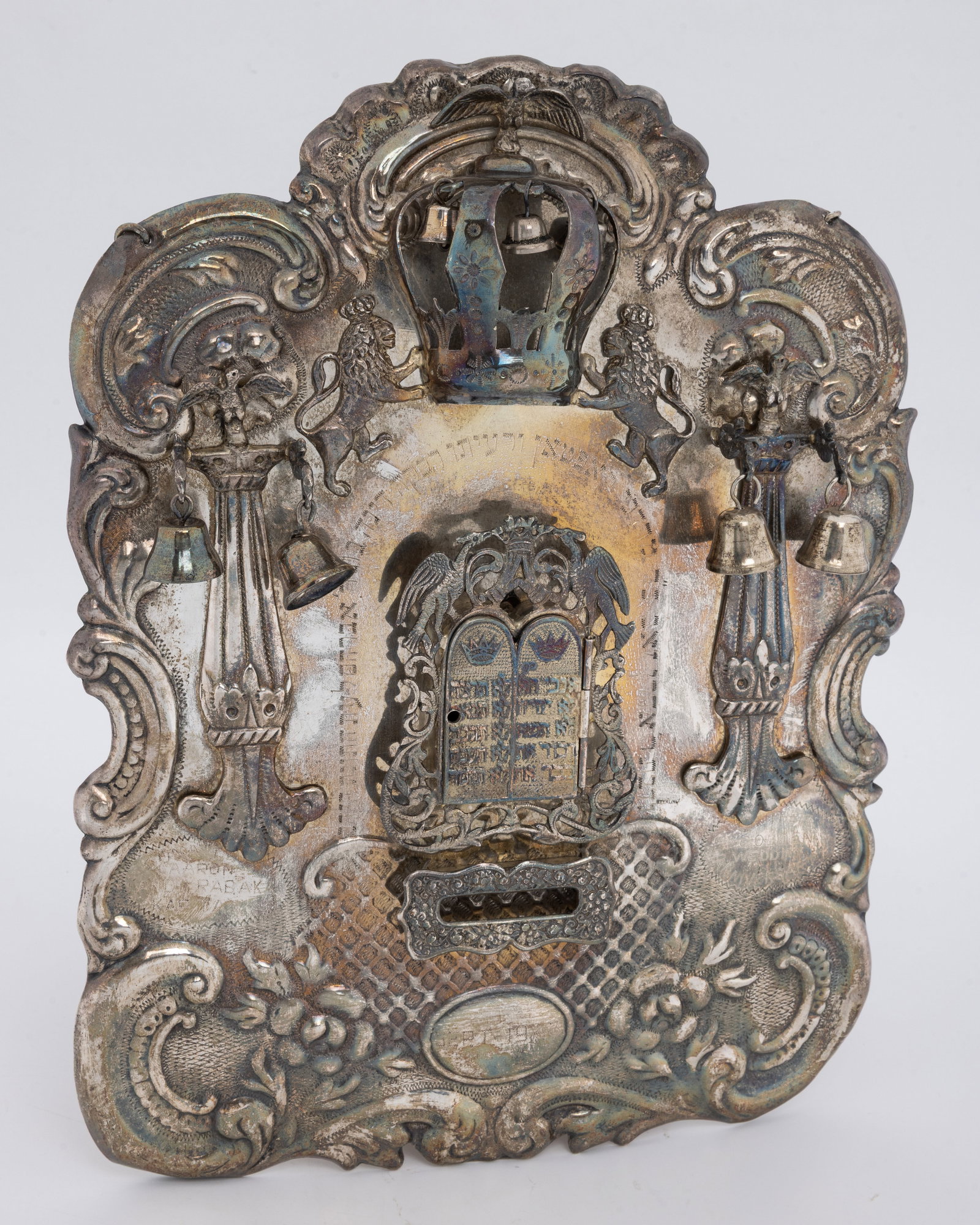 A LARGE STERLING SILVER TORAH SHIELD. American, 1943: Traditional form. Decorated with embossed lowers, pillar, bells, a crown, lions, bells and an ark. Engraved with a dedication dated to September of 1943 on the anniversary of Aron and Rabaka Kaplan. 1