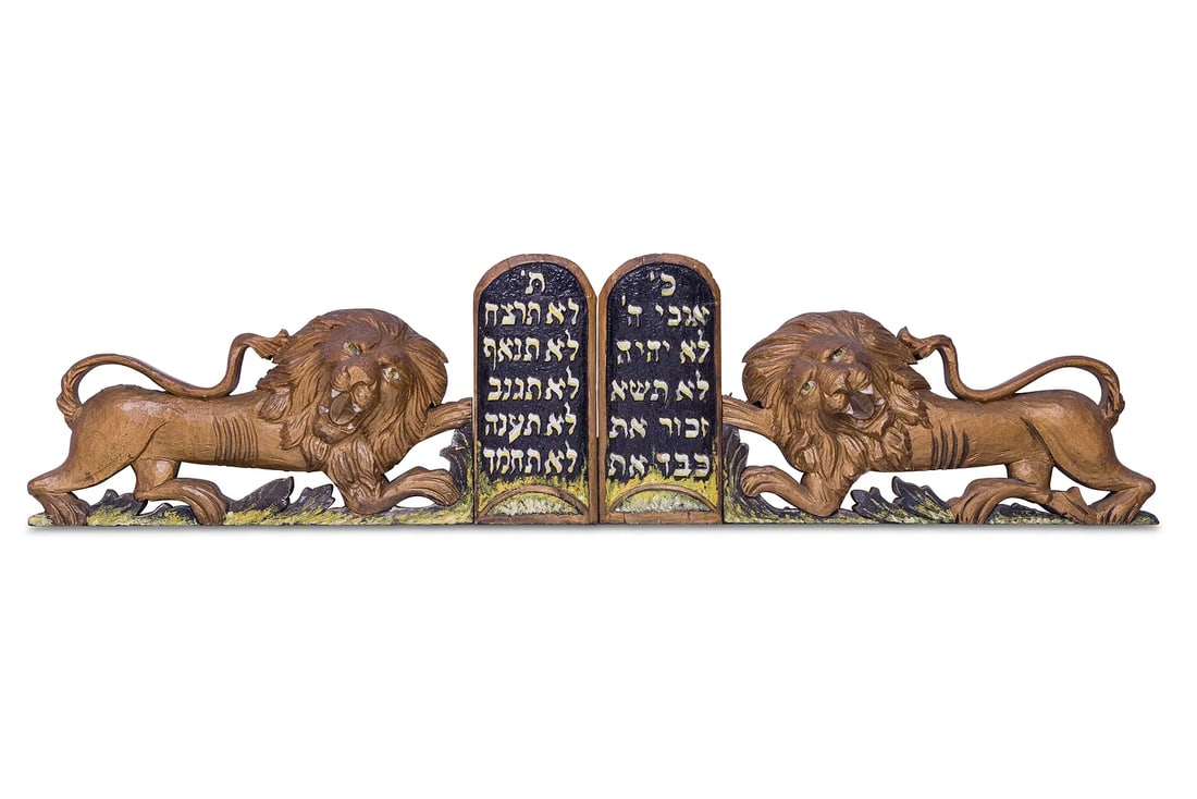 A LARGE PAIR OF HAND CARVED WOODEN LIONS FROM AN ARON KODESH.: United States, c. 1900. The lions are gilded and are flanking a Decalogue with a painted background. Painted with yellow enhancements along the base. 65” x 17”.Minor losses, repairs and