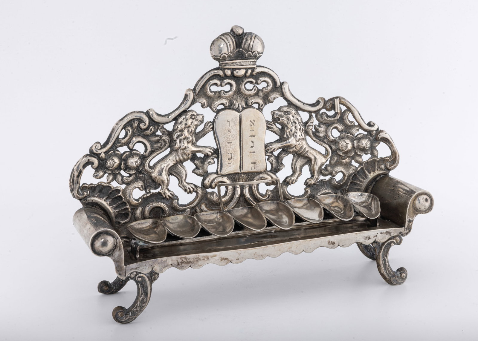 A SOFA SHAPED SILVER HANUKKAH LAMP. Vienna, Austria, 1842.: The body is in the form of a sofa. The backplate hand chased and cut with two lions flanking a decalogue, Scrolls, flowers and a crown. Of exceptional gauge and quality. The spoon shaped oil holders
