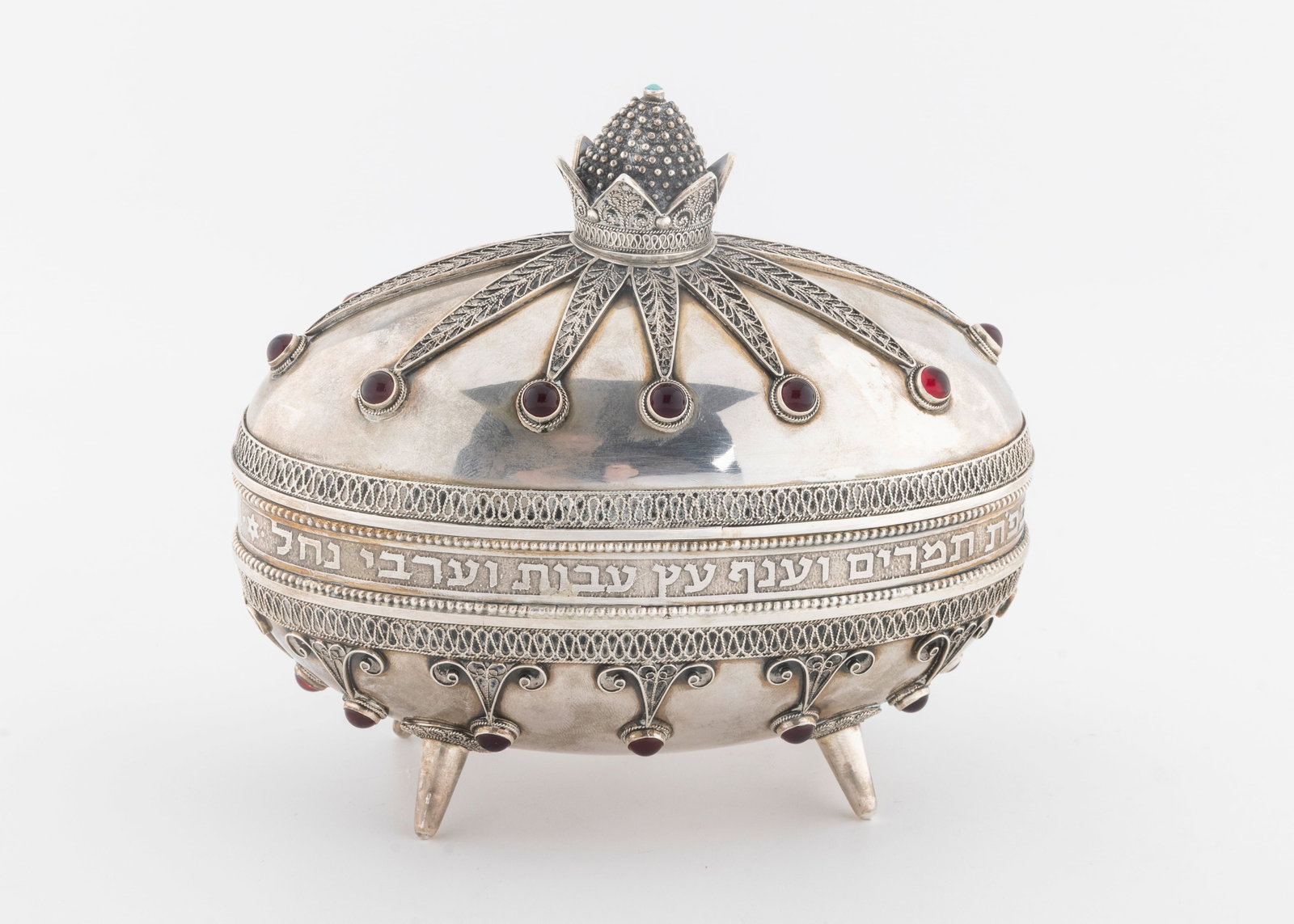 AN IMPORTANT SILVER AND GARNET ETROG CONTAINER BY YAKOV YEMINI. Jerusalem, c. 1980: On four pole legs. In oval shape. Decorated with applied filigree, wire work, garnets and acid etched scriptural excerpt relating to the Succoth holiday. Signed. 6.5" wide