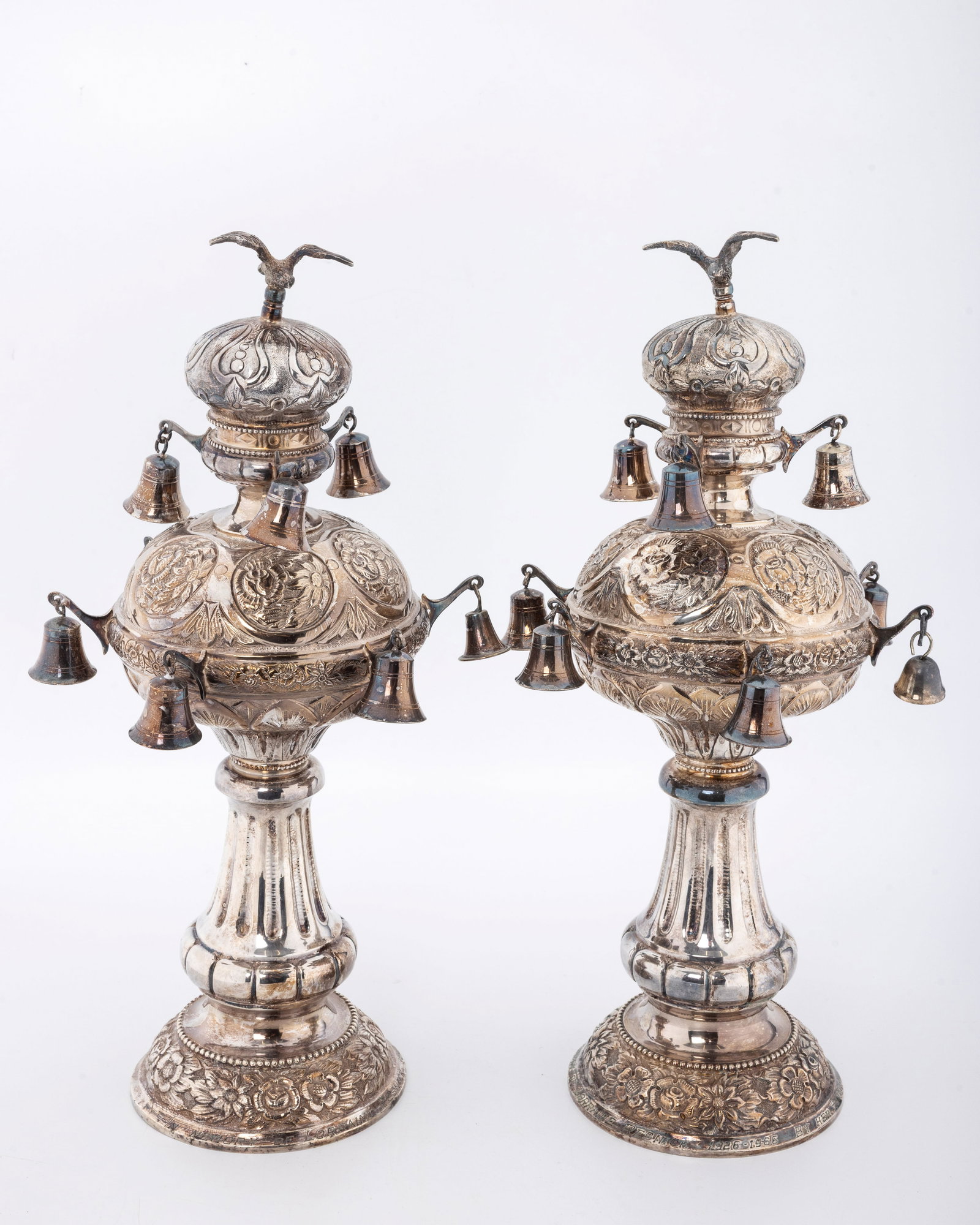 A PAIR OF SILVER TORAH FINIALS. Hungarian, mid-20th century: On round bases chased with floral decoration. The main body is columnar is shape. The upper portion in matching decoration. Each topped by a bird. Inscribed on the base with a dedication inscription
