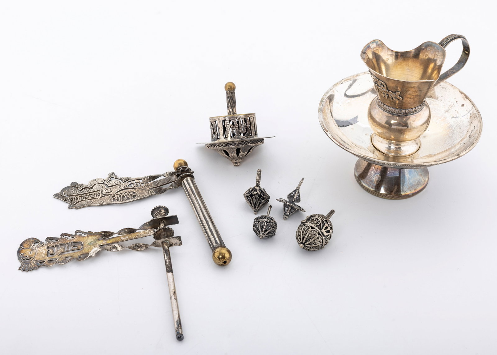 A GROUP OF FIVE DREIDELS, A MAYIM ACHRONIM AND TWO GRAGGERS.: Probably Israel, modern. The graggers are over 4" tall each. The largest of dreidels has a brass upper portion, the rest sterling silver. Total weight is 237 grams