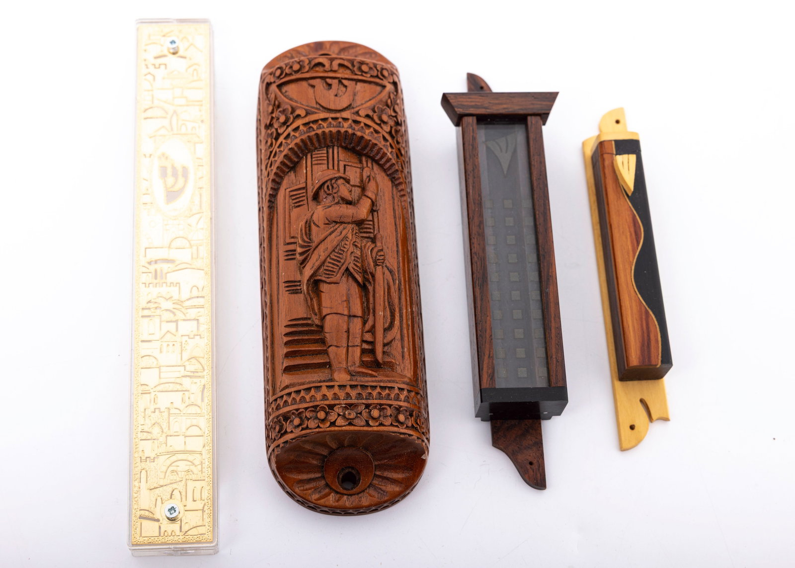 A GROUP OF FOUR MEZUZOT COVERS.: Including a hand carved model depicting a young boy putting up a mezuzah on a doorpost, a Jerusalem scene one and two others.