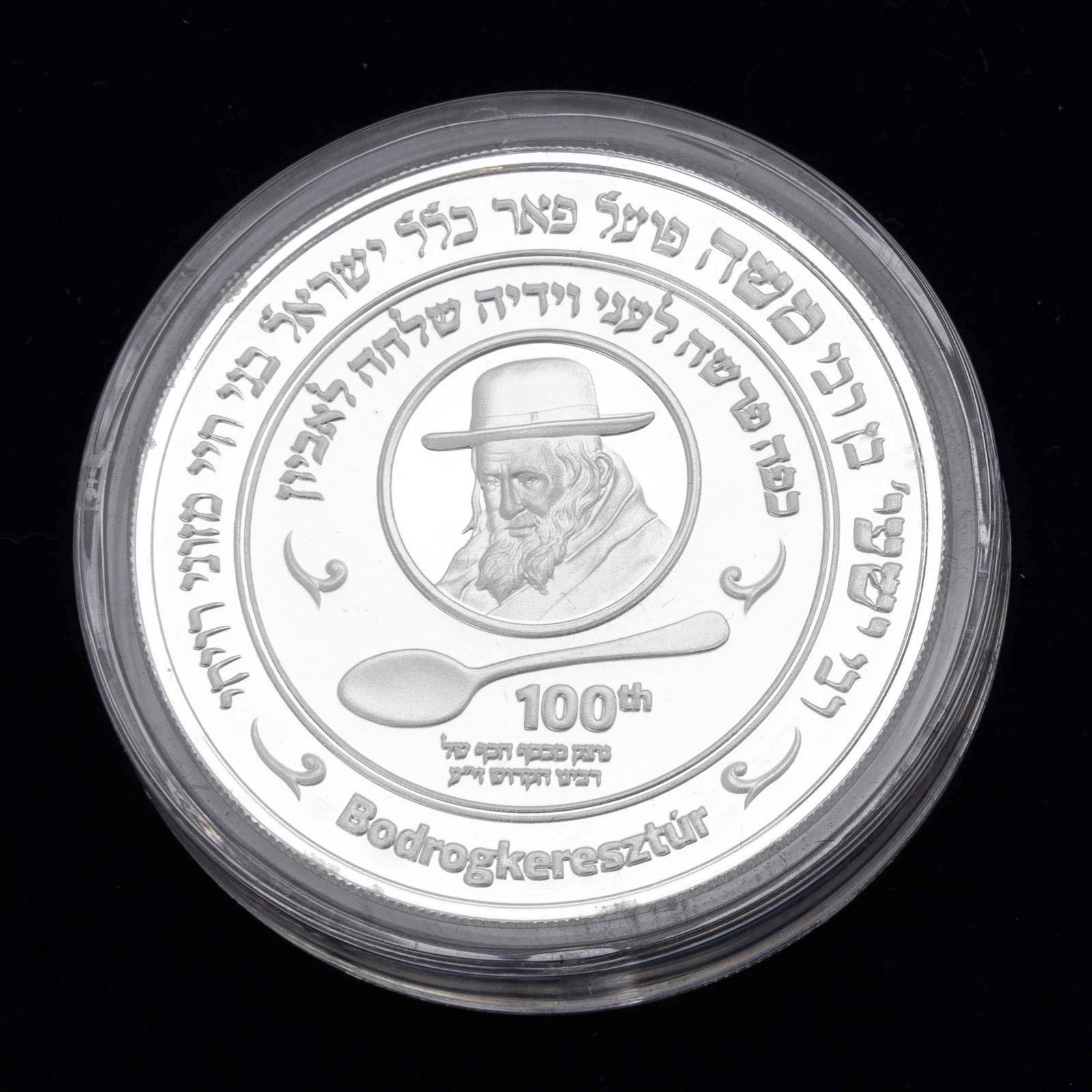 A SILVER COIN MADE IN HONOR OF REB SHAYALA OF KERISTIR WITH HIS HOLY SILVER.: A historic commemorative coin of the Holy Rebbe Yeshaya Steiner of Kerestir. Minted in New Zealand, 2024 from 2 ozt of silver. Limited edition of 700 pieces. It encompases silver from a spoon used by 