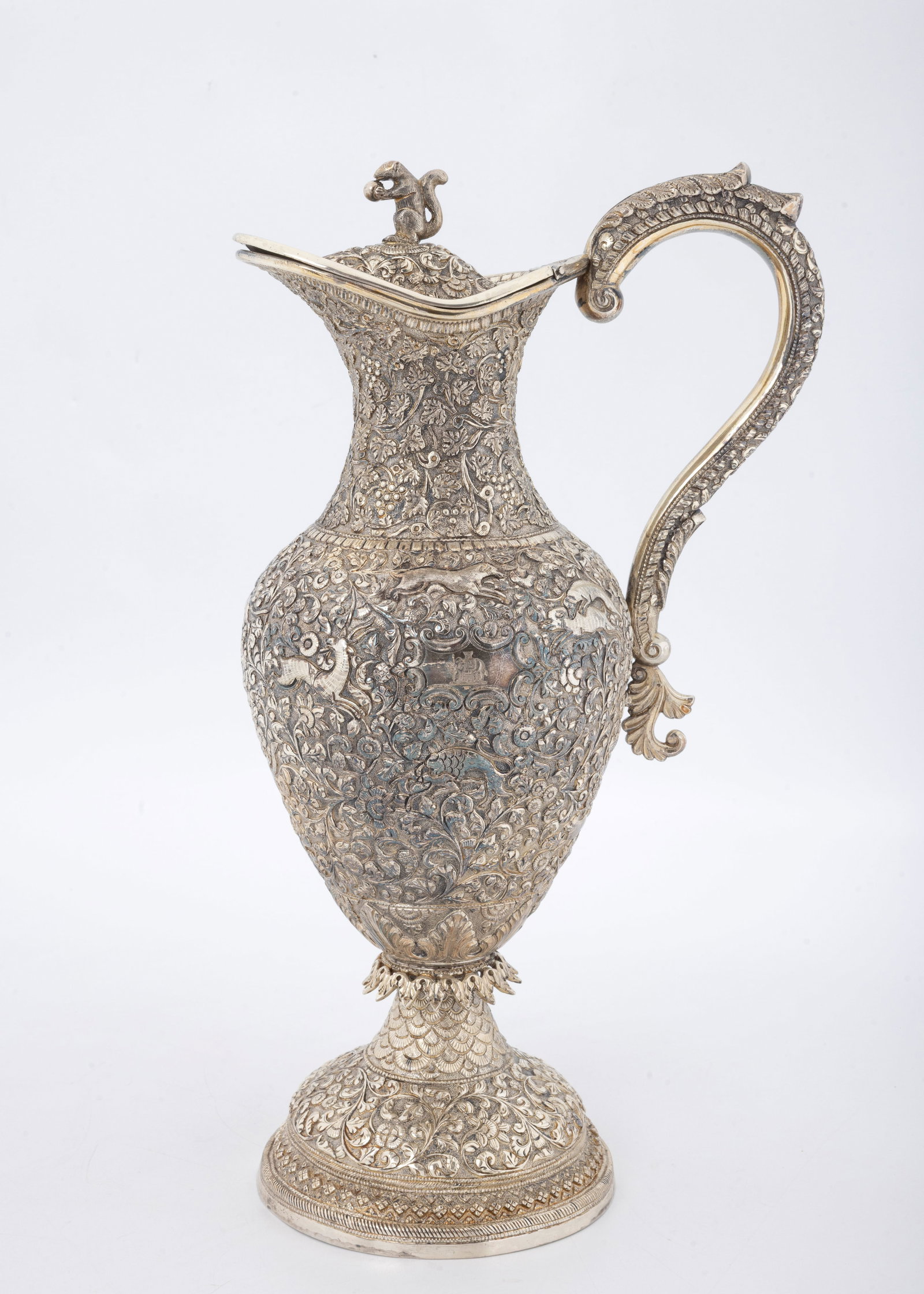 A MAGNIFICENT INDIAN COLONIAL SILVER WINE CLARET JUG. India, c. 1880: Kutch(Cutch)/Gujarat or Kashmir. c. 1880. Intensely chased with antelope, dogs, foxes, a hunter, a bull and other animals, many in hunting stages. Topped with a squirrel finial. The body and neck are