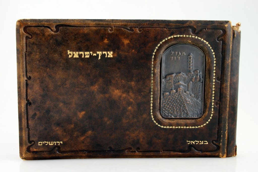 AN EARLY BEZALEL PICTURE BOOK. Jerusalem, c. 1920. Leat: AN EARLY BEZALEL PICTURE BOOK. Jerusalem, c. 1920. Leather bound with bronze medal of Migdal David and many lithographs of Zev Raban of the Holy Land. 8” wide.