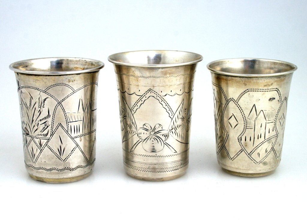 THREE LARGE SILVER KIDDUSH BEAKERS. Russian, 19th centu: THREE LARGE SILVER KIDDUSH BEAKERS. Russian, 19th century. Engraved with foliate decoration and shetetel scenes. 2.8” tall.