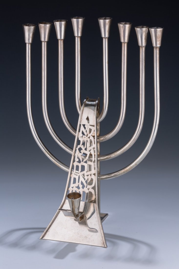 A LARGE STERLING SILVER MENORAH. Portugal, c. 1970. In: A LARGE STERLING SILVER MENORAH. Portugal, c. 1970. In the style of David Gumbel. Cut with Hebrew wording related to Chanukah. 12.7” tall.