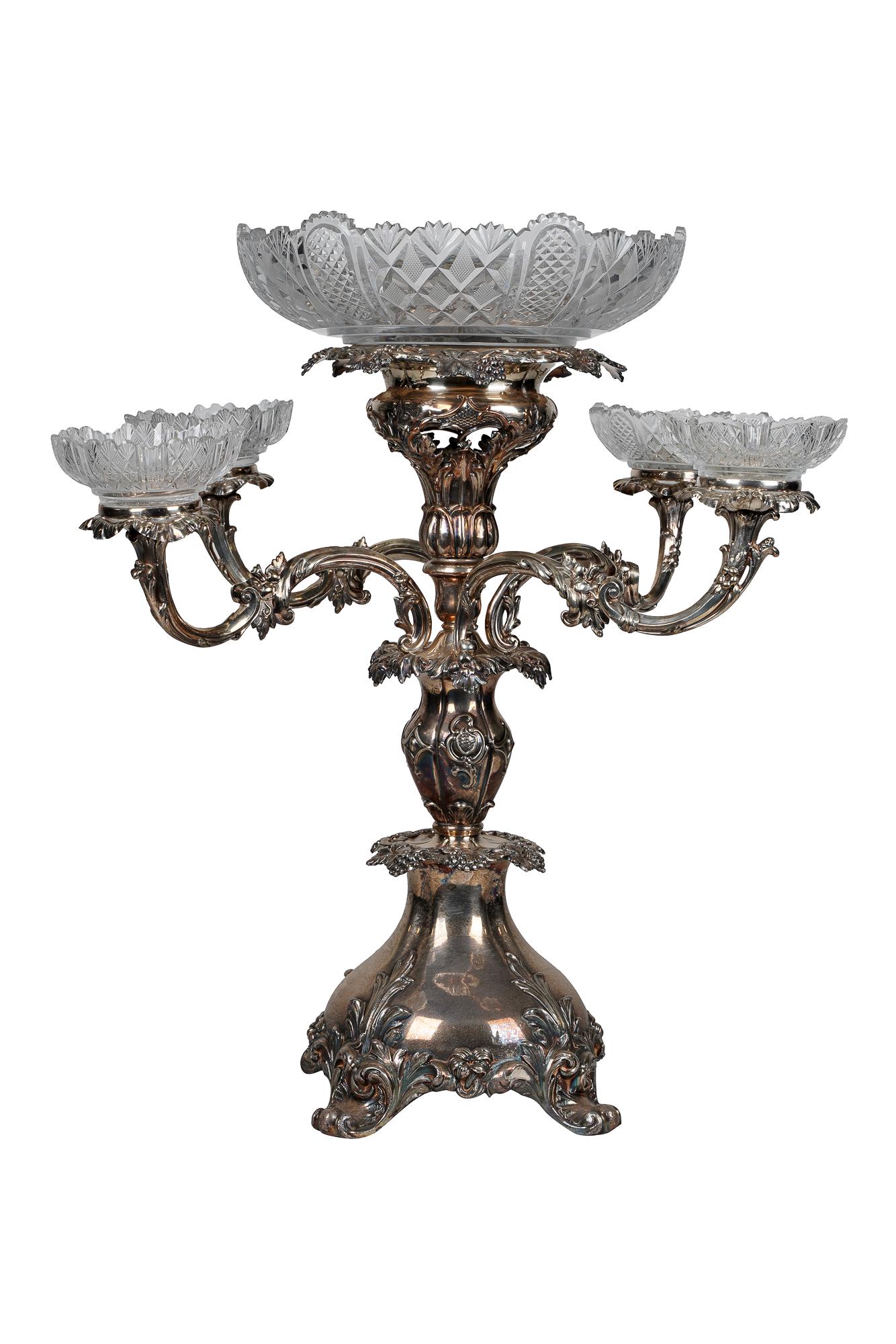 SILVERPLATE EPERGNE: with four removable arms apparently unmarked Condition: one cut glass insert is a replacement in a different pattern from the others. Scattered dings. Bending to rims of central support and two second