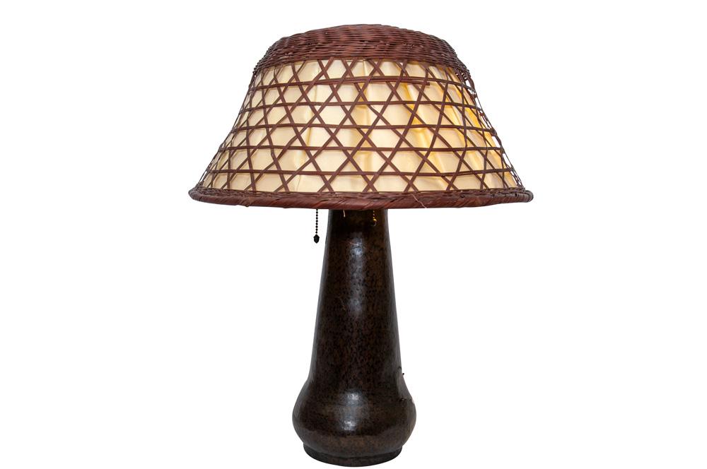 GUSTAV STICKLEY TABLE LAMP: circa 1910 hammered copper base with linen and wicker shade of a different maker condition: with slight loss and breaks to shade 23 total inches high; shade 18 inches diameter; 9 inches high