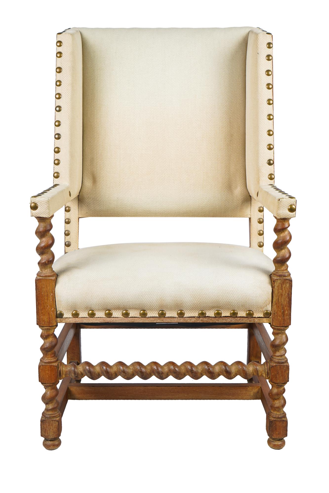 JEAN MASCHERONI CARVED OAK WING CHAIR: with beige herringbone-pattern upholstery with large nail heads Condition: Frame in good condition. General light dust accumulation to fabric. Stains to seat. Some wear to front corners of armrests. 2