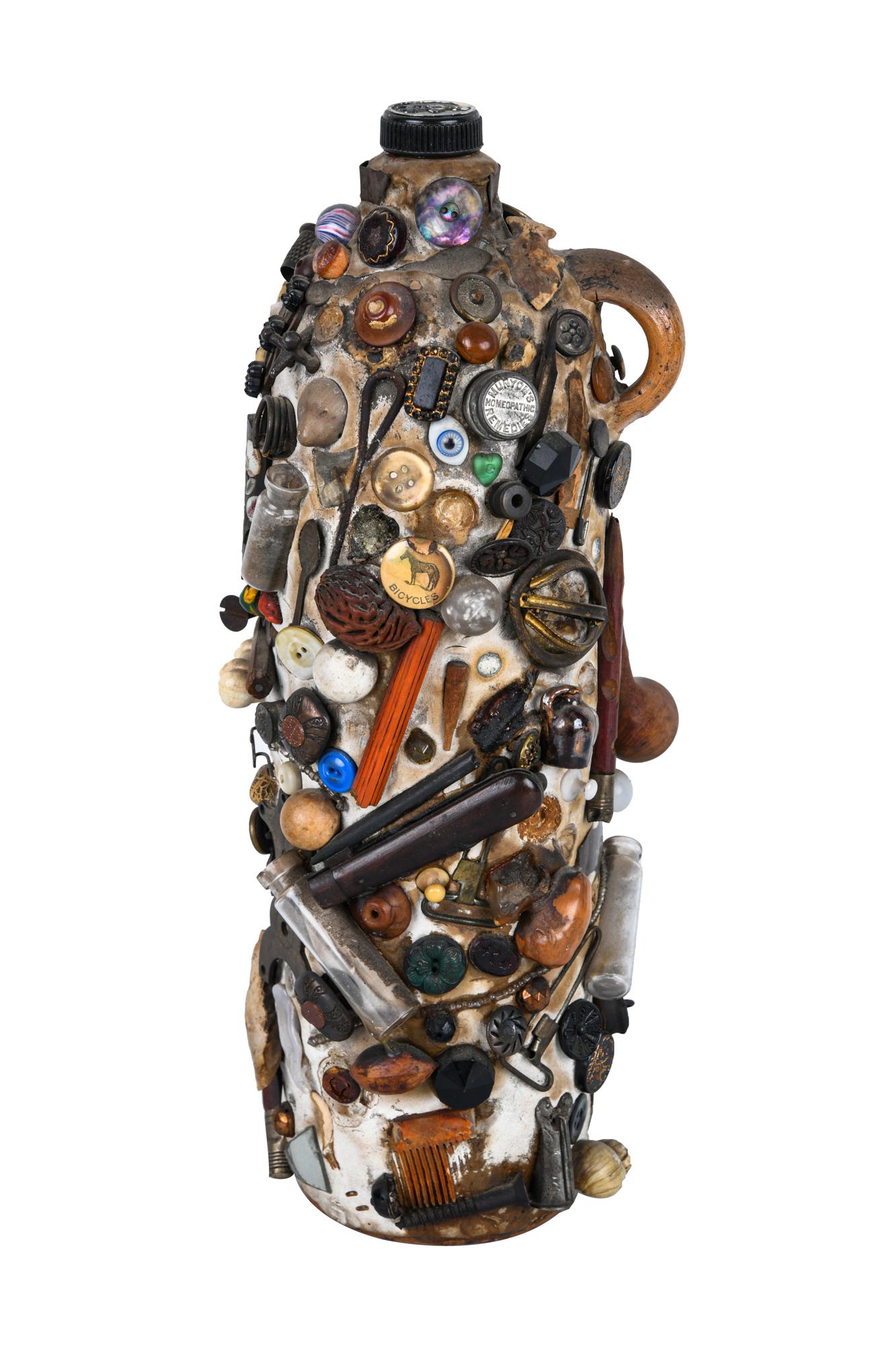 MOSAIC FOUND OBJECT JUG: earthenware jug coated in epoxy and decorated with found objects objects including: pins, buttons, glass vials, jacks, spoons, screws, an arrowhead, etc. Condition: with pieces missing 12 1/2 inches h
