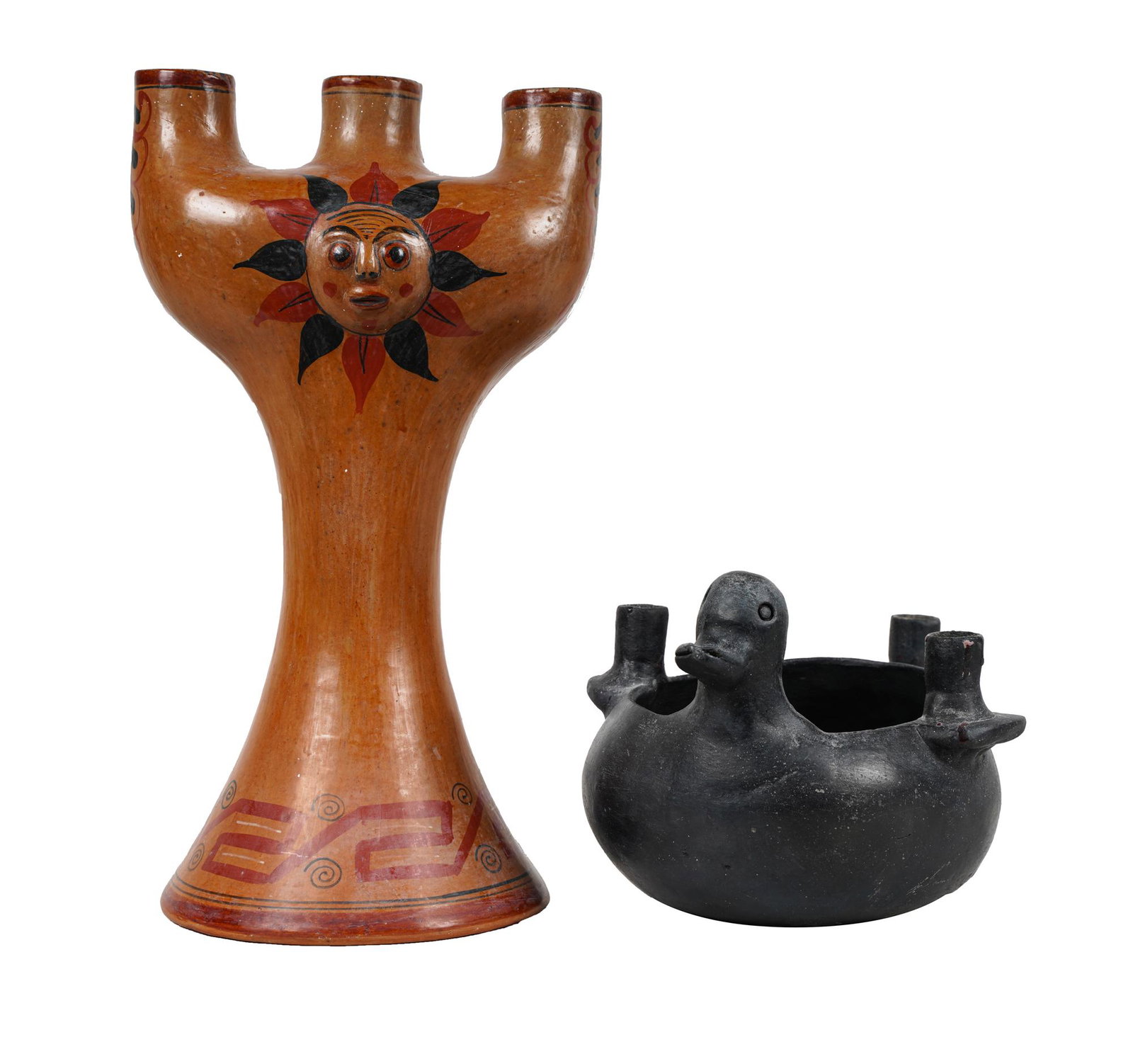 TWO MEXICAN CERAMIC CANDELABRA: the first: unsigned, black-glazed, duck-form with three sockets and an open center; the second: inscribed to underside "Mexico FLP", with red and black sun motif decoration on a buff-colored ground, w