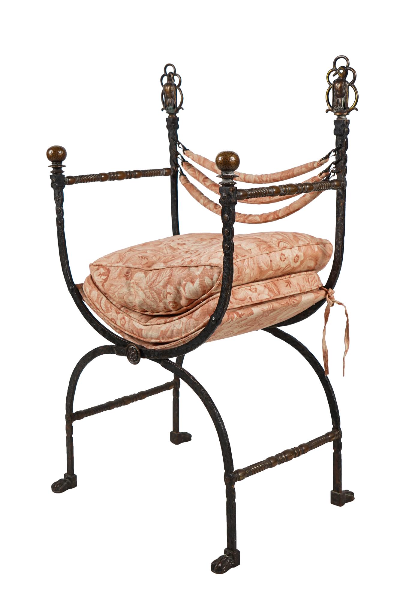 WROUGHT IRON & BRONZE CURULE CHAIR: circa 1920, in the manner of Oscar Bach with bird-form finials and claw feet, the later suspended seat and back supports of red and cream-colored fabric, with matching loose cushions Condition: the se
