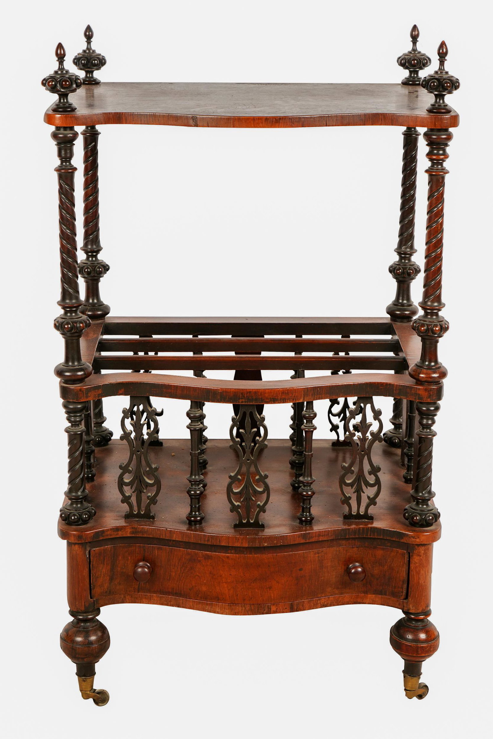 EDWARDIAN MAHOGANY CANTERBURY: with serpentine top and lower shelf fitted with two dividers, over a drawer, raised on metal casters Condition: wear and marks to finish of top. 22 inches wide; 16 inches deep; 38 1/2 inches high