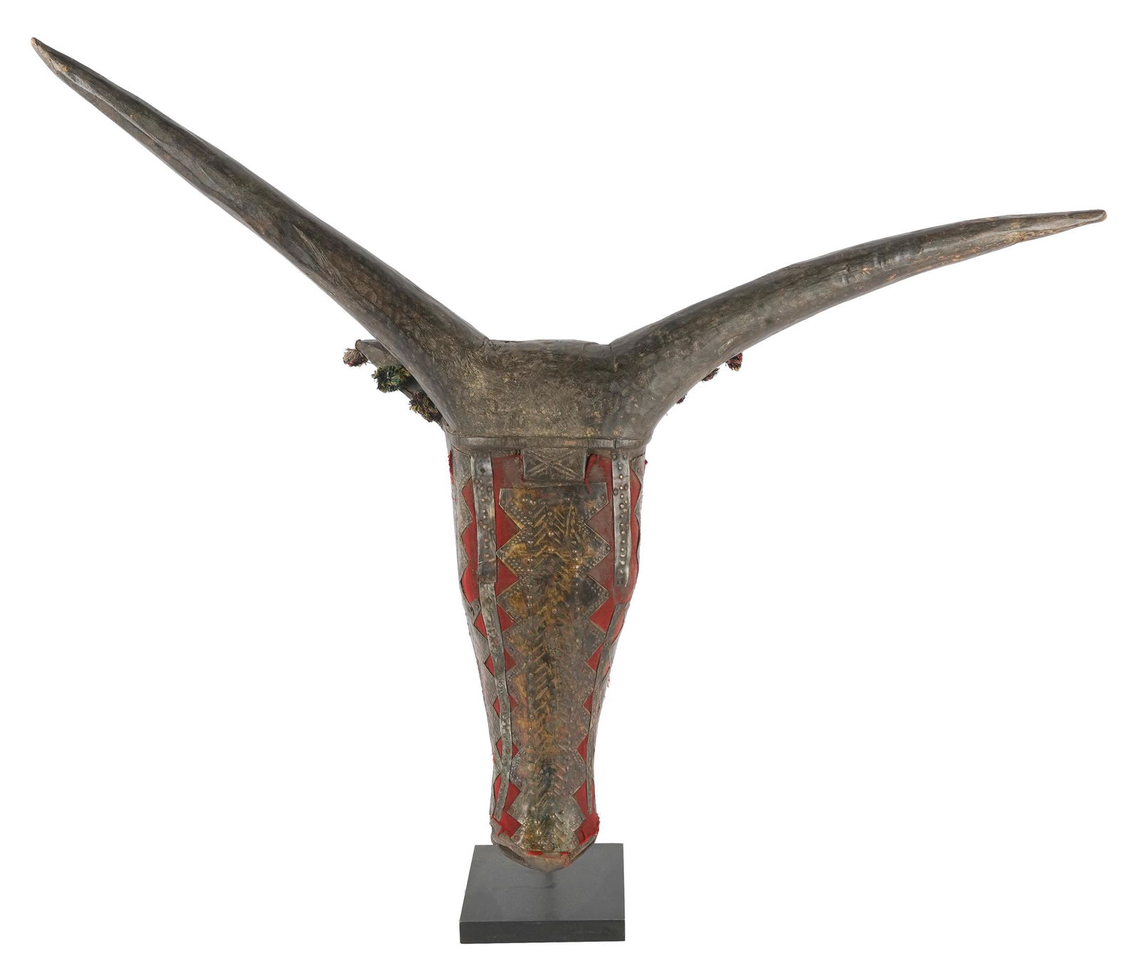 PAINTED WOOD CARVING: modeled as an animal's head and inset with metal and red fabric; on a metal and wood stand; 37 inches wide; 8 inches deep; 32 inches high
