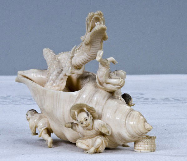JAPANESE CARVED IVORY GROUP: depicting a dragon emerging from a shell with four applied figures 4 3/4 inches