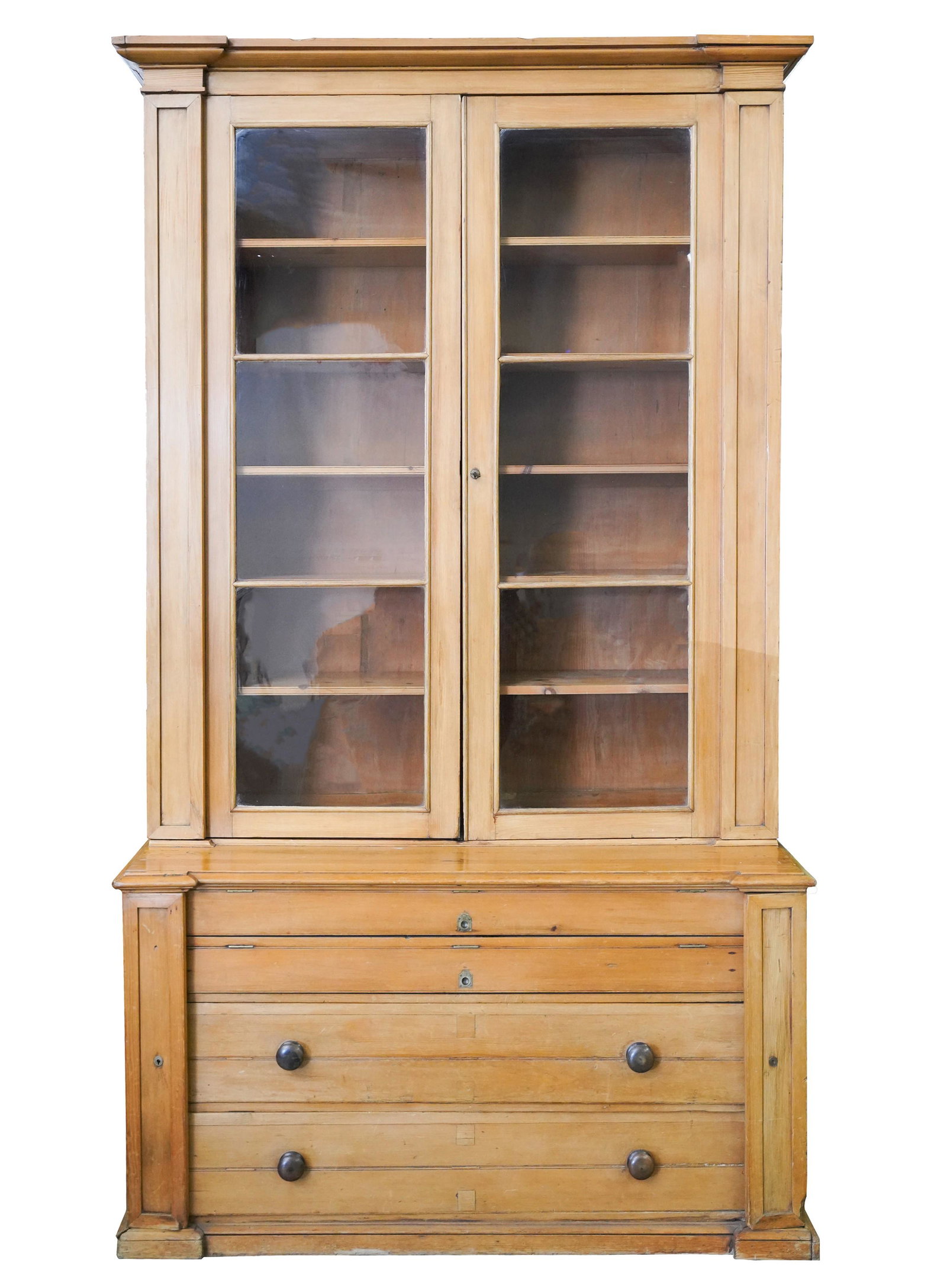 Louise Fletcher- Antique Pine Cabinet: 19th / early 20th century; constructed in two parts; the upper case with glazed doors enclosing five shelves; the outset lower case with two full-width slides over two full-width drawers, flanked by l
