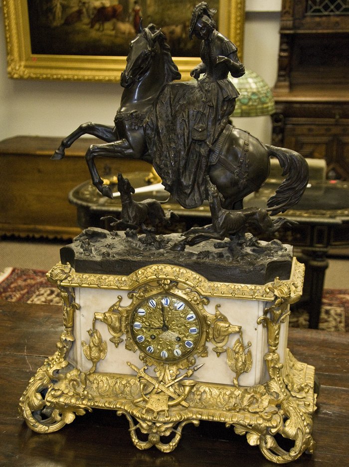 FRENCH BRONZE, GILT BRONZE, AND MARBLE FIGURAL MAN: the surmount of a lady astride a horse with dogs on a ivory marble base with central clock face and ormolu mounts 20 inches wide; 28 1/2 inches high