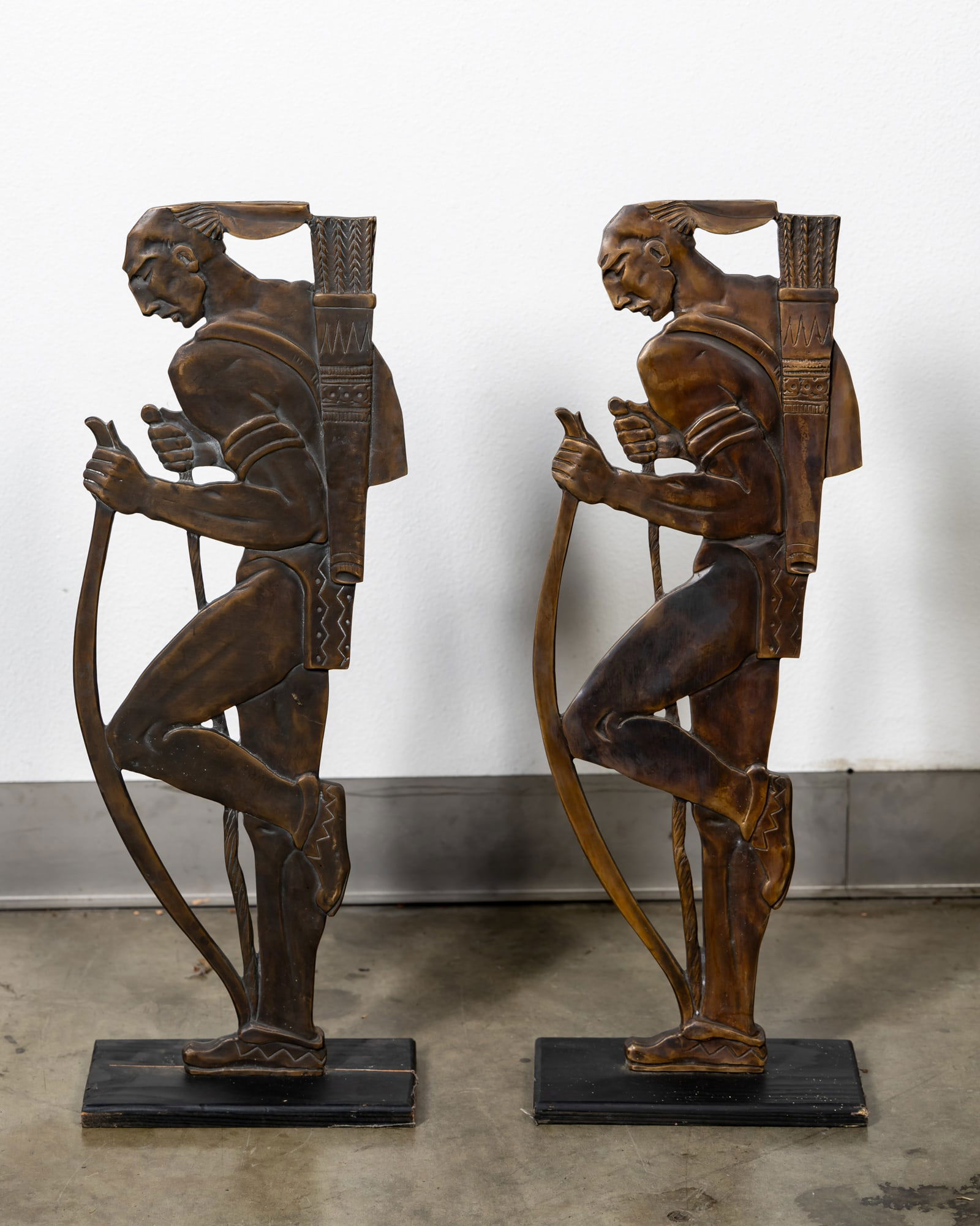 Two Native Americans with Bow and Arrow Bronze Table Bases: with two drill holes to the top of the head, mounted to wood, 31 x 11 x 6 in. (78.7 x 27.9 x 15.2 cm.) Provenance: The Private Collection of Robin Chretien, founder of Robin's Jean