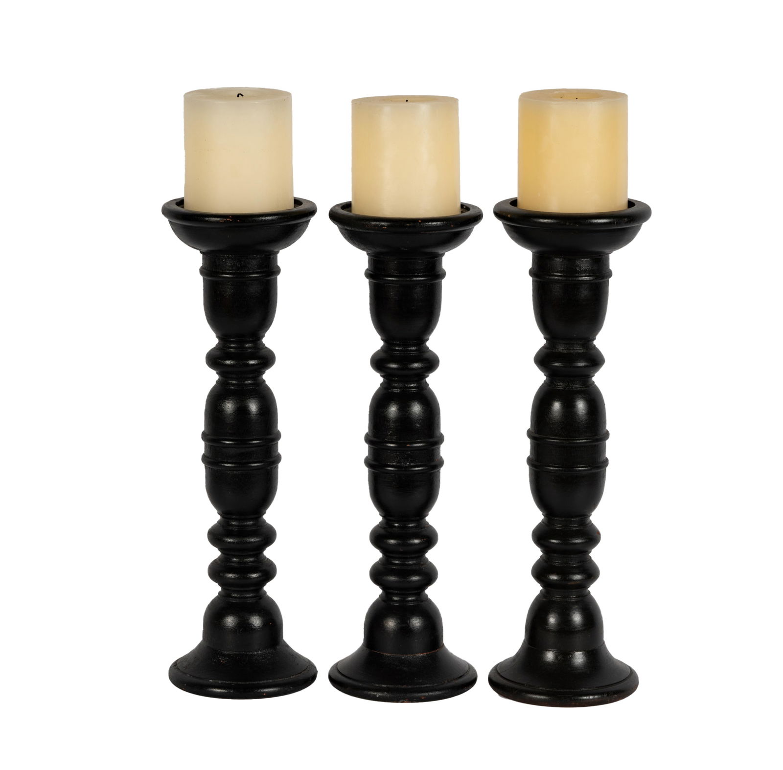 A Set of Three Ebonized Wood Candlesticks: unmarked; together with three wax pillar candles Excluding candles: 17 3/4 in. (45.1 cm.) high