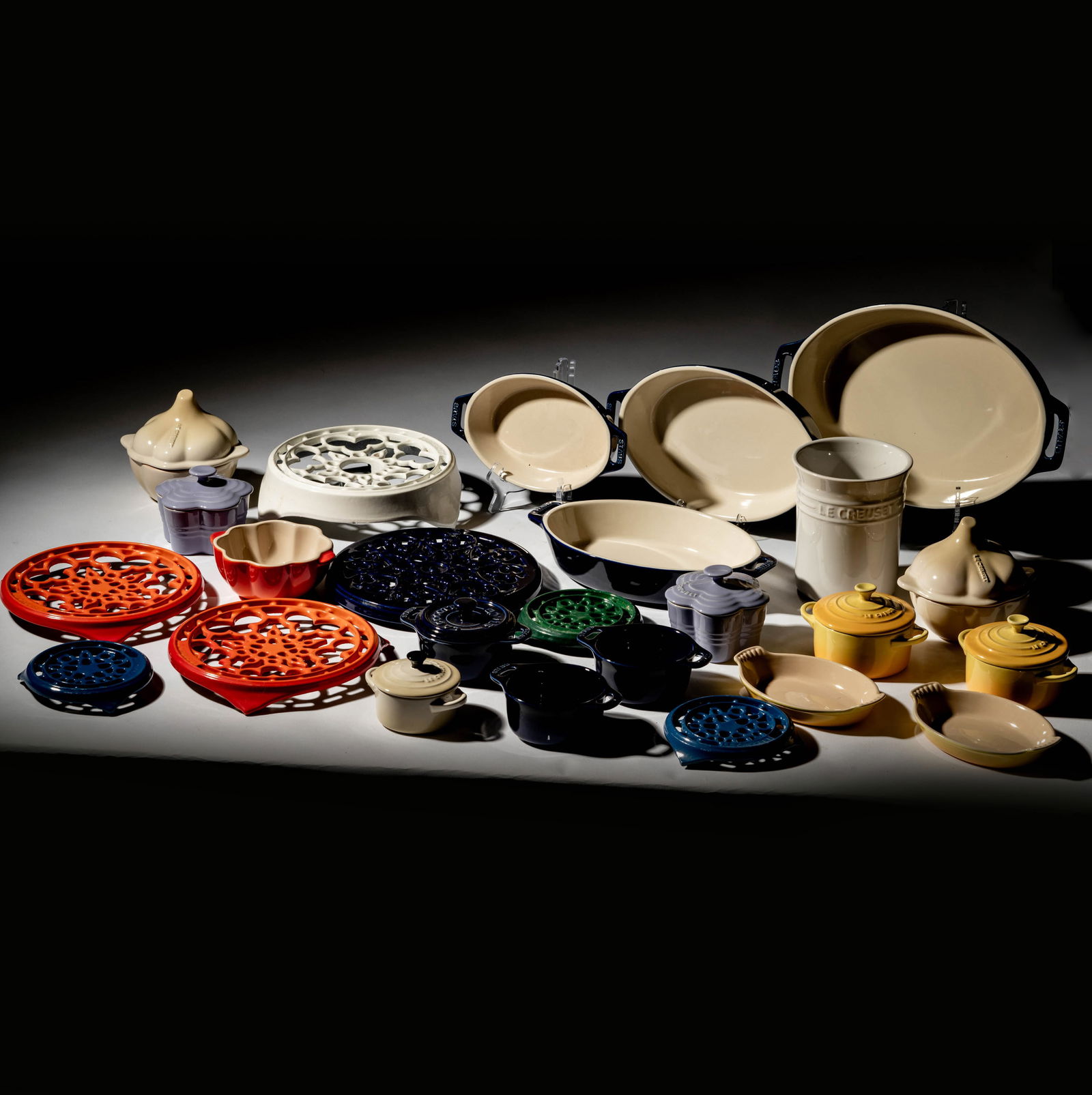 A Group of Le Creuset and Staub Ceramic Bakeware: comprising 18 pieces, including an oval casserole: 14 in. wide); together with seven enameled cast iron trivets Largest trivet: 9 in. dia.