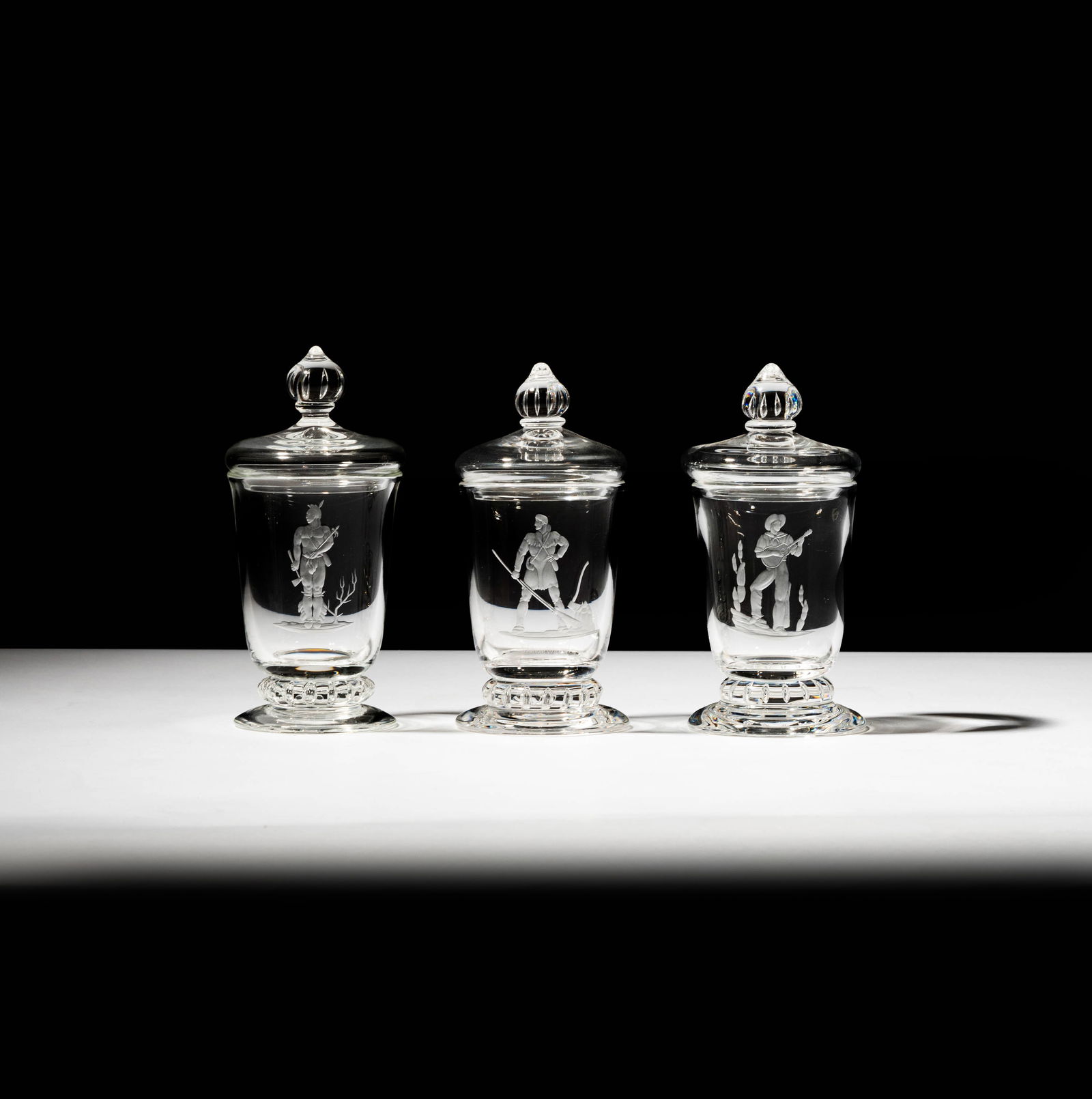 Set of Three Steuben Glass Covered Urns: from "The American Ballad Series", comprising: "The Indian", "The Cowboy", and "The Pioneer", each designed by Sidney Waugh; each signed; "Indian": 6 in. (15.2 cm.) high; "Cowboy" and "Pioneer": 5 3/4