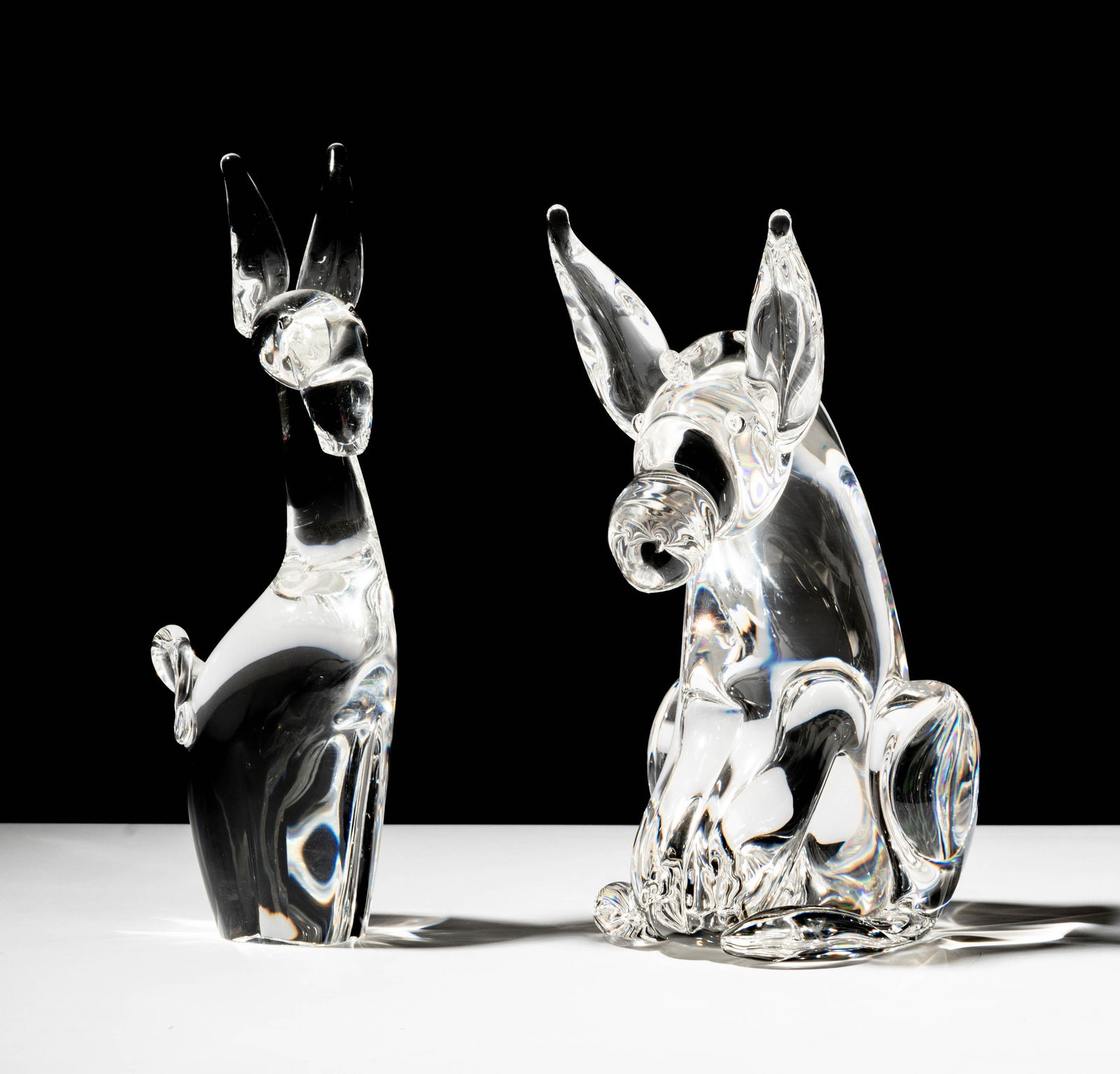 Two Steuben Glass Donkey Sculptures: each signed; Standing figure: 10 1/4 in. (26 cm.) high; Seated figure: 9 1/2 in. (24.1 cm.) high; Provenance: The collection of Santa Barbara Steuben collector Joel Kreiner