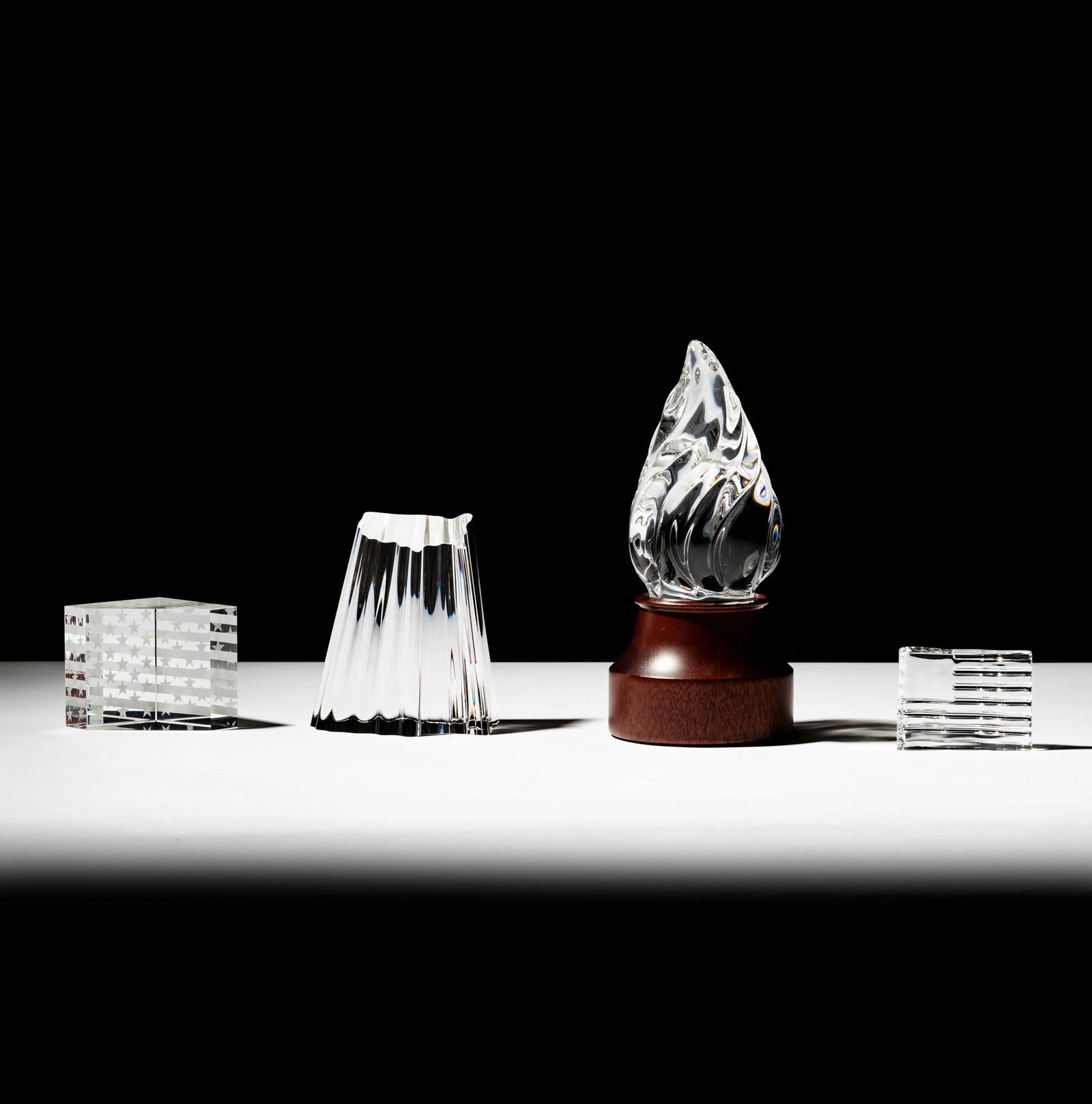 Four Steuben Glass Table Ornaments: "Torch of Strength", United States territory, and two flag sculptures; each signed; Ranging from: 8 in. high (20.3 cm.); To 2 in. high (5.1 cm.); Provenance: The collection of Santa Barbara Steuben co