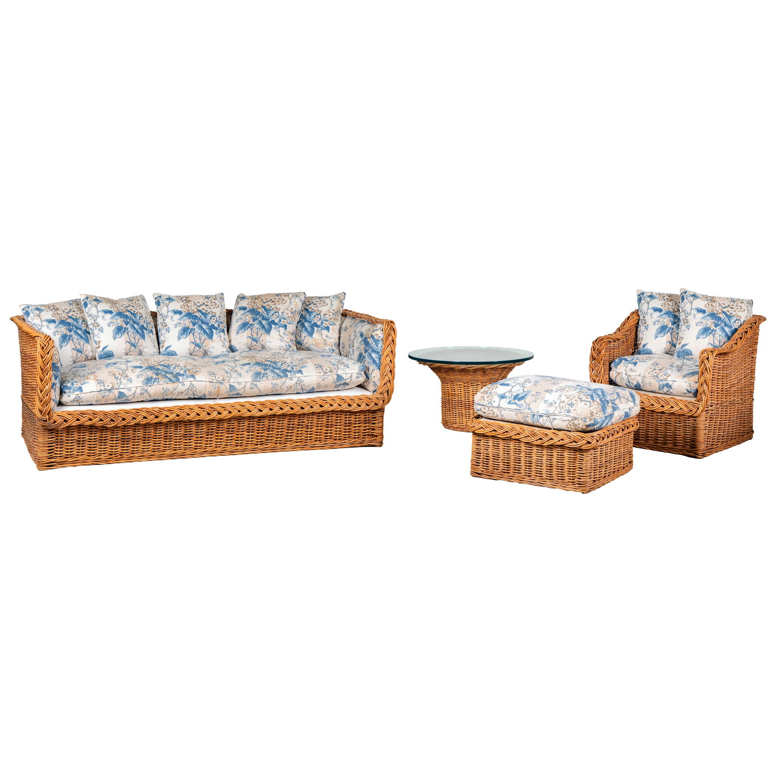 A Wicker Furniture Suite with Brunschwig et Fils Fabric Cushions: comprising a sofa (29 x 84 x 39 in., Seat height including cushion: 18 in.), an armchair (29 x 33 x 32 in.), an ottoman (16 x 28 x 23 in.), and a round end table with glass top (18 x 30 in.); with man