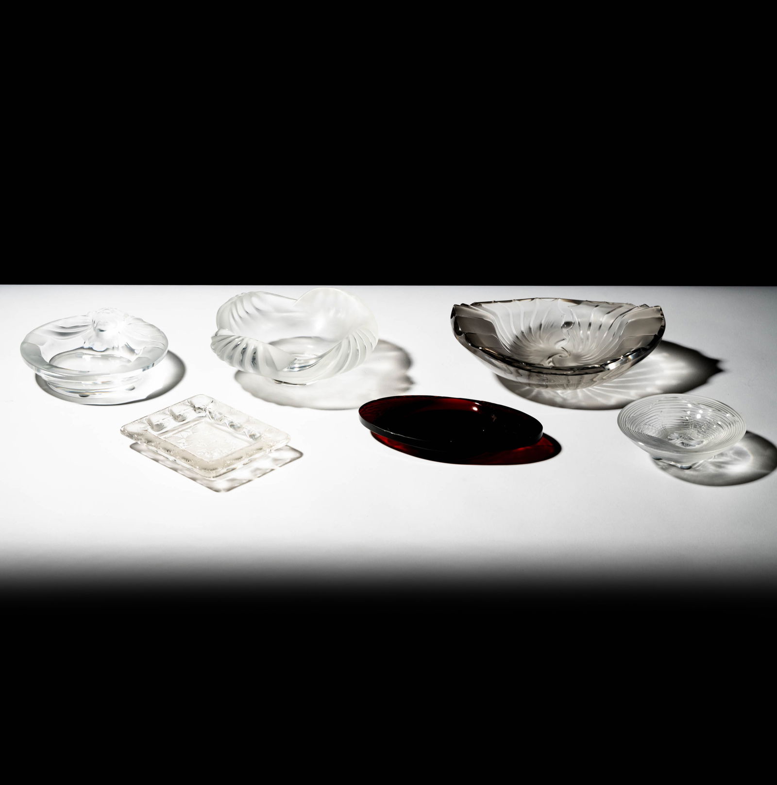 A Group of Lalique Glass Ashtrays: comprising five in clear and frosted glass, each signed "Lalique France" (Ranging from 4 5/8 in. dia. to 8 1/2 x 6 7/8 in.); together with one oval in amber-colored glass signed "R. Lalique" (6 3/4 x