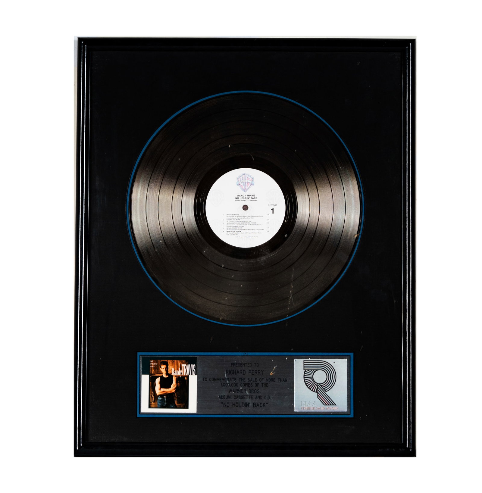 Richard Perry's Platinum Record Randy Travis 'No Holdin Back': This framed award commemorates the sale of over 1,000,000 copies of Randy Travis' Warner Bros. album, cassette, and CD, 'No Holdin' Back'. It features the album cover, a vinyl record, and the RIAA Cer