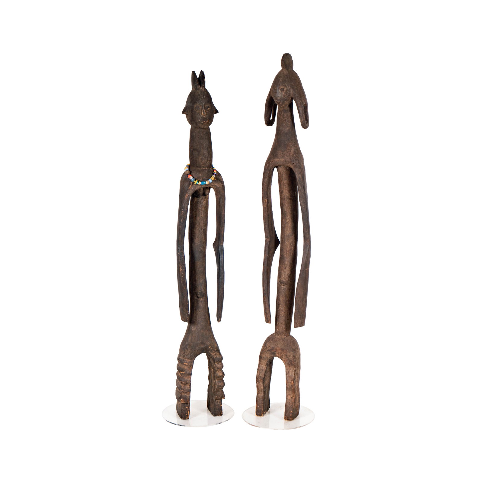 Two African Wood Carved Sculptures: each set on acrylic bases, Larger: 60 x 7 x 4 1/2 in. (152.4 x 17.8 x 11.4 cm.), Smaller: 57 x 6 x 5 1/2 in. (144.8 x 15.2 x 14 cm.)