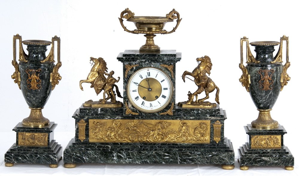 FRENCH ORMOLU MOUNTED MARBLE CLOCK GARNITURE: FRENCH ORMOLU MOUNTED MARBLE THREE-PIECE CLOCK GARNITURE the Neoclassic style clock with an urn-form finial and enameled face signed "Britthazard Paris" flanked by Marly horses and a bronze bas-relief