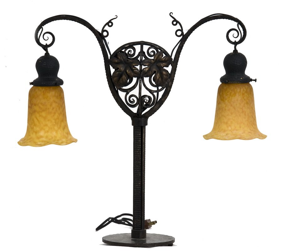 DAUM NANCY CRYSTAL & WROUGHT IRON TABLE LAMP: the narrow neck branching from the round hammered base into an open wrought iron vine and leaf design and two vine form arms each with signed orange glass bell shade 20 1/2 inches high; 22 inches long