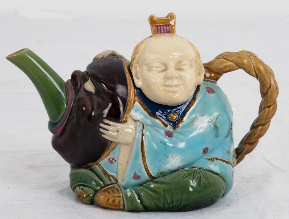 MINTON MAJOLICA "CHINAMAN" TEAPOT: circa 1874 the molded pot in the form of a man holding a mask from which extends a spout, the man's head forming the lid, his braid the handle; in shades of blue, green, purple, and wheat; inscribed 1